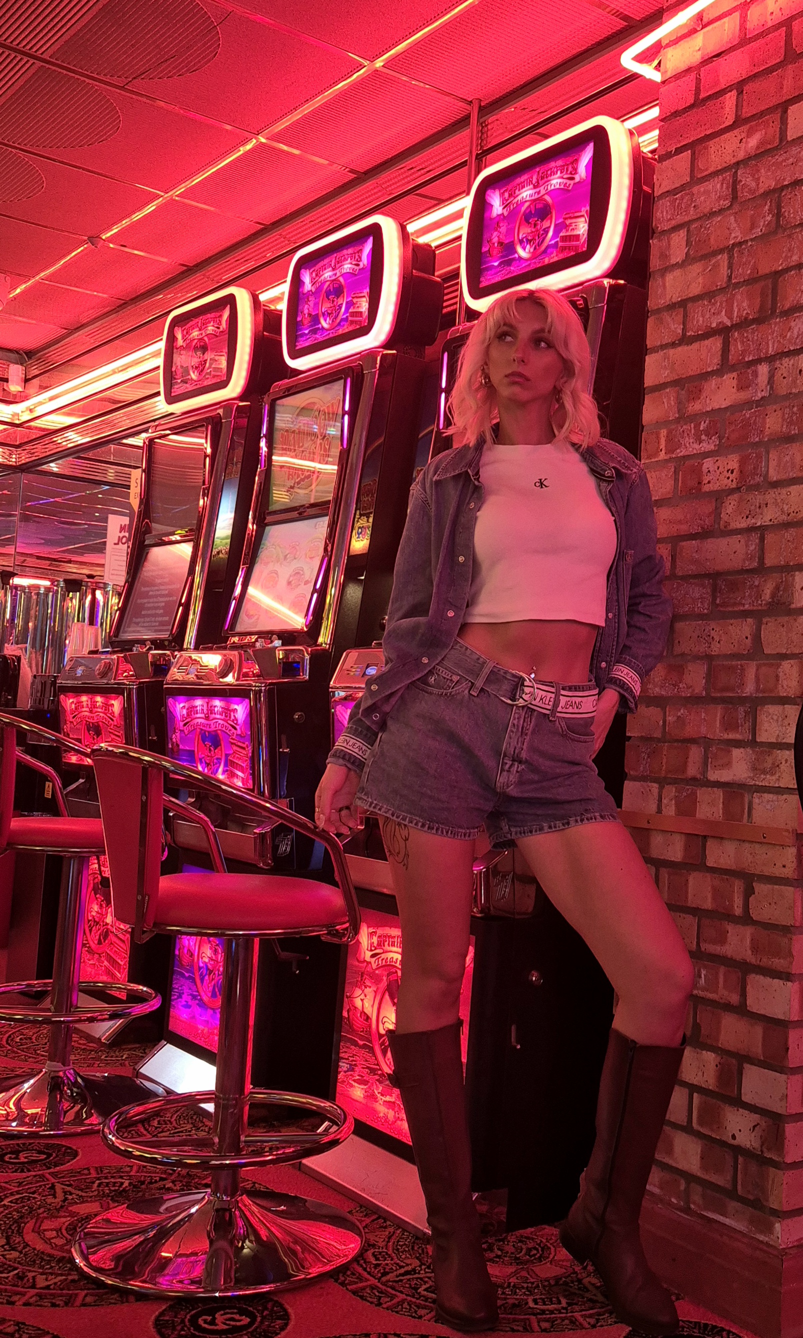 Emma under pink neon arcade lights in denim and a white crop top